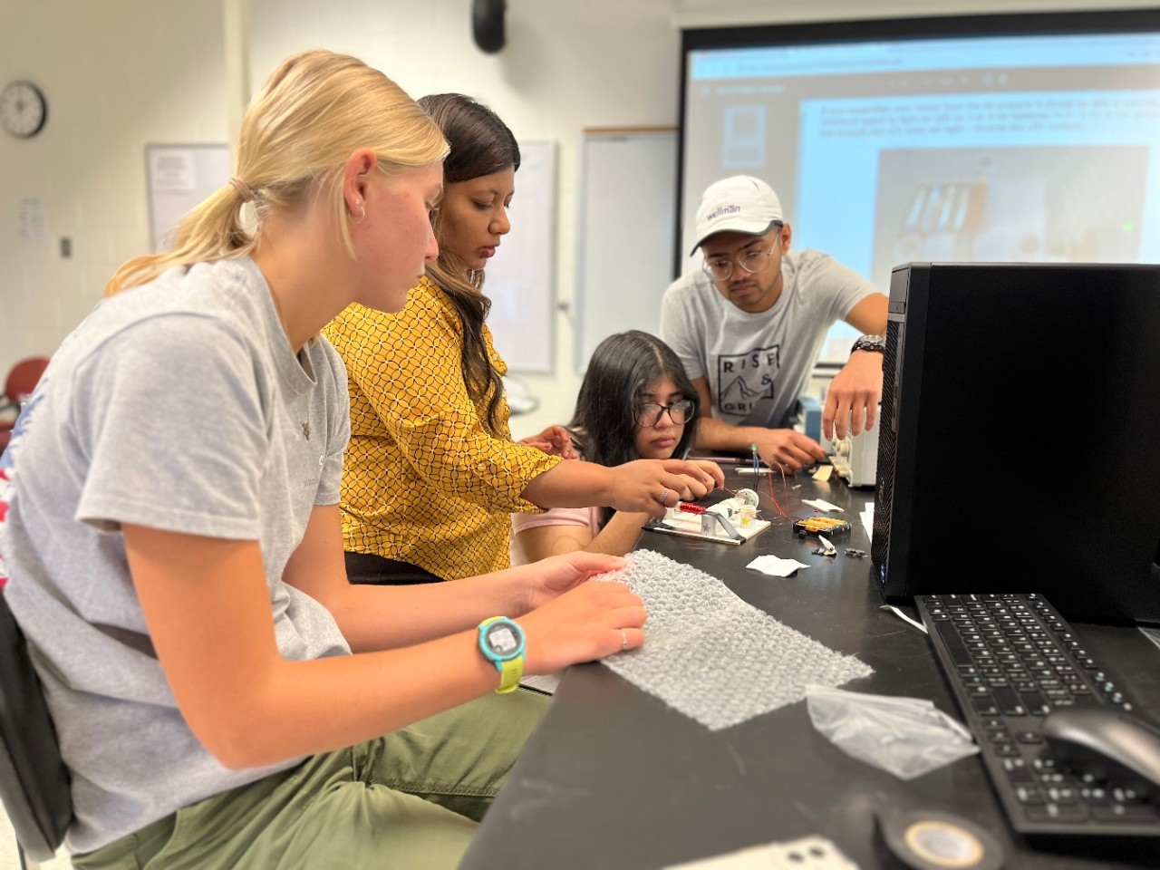 Electrical and Electronics Engineering Academy High school aged students watching intently as academy leader assists with an engineering project